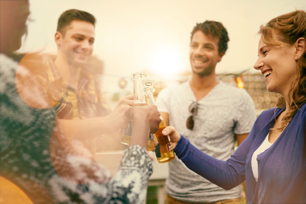 Multi-ethnic millenial group of friends partying and enjoying a beer on rooftop terrasse at sunset