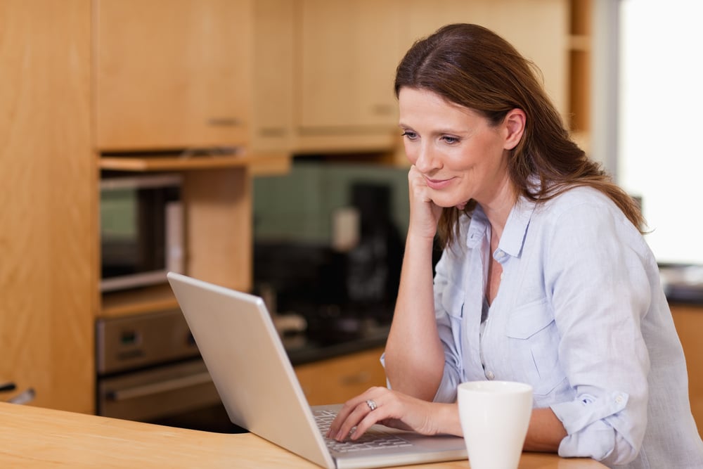 Smiling woman in the kitchen looking at her laptop-1